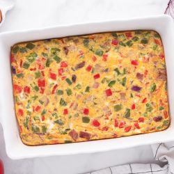 Breakfast egg casserole with turkey bacon, cheddar cheese, peppers, and onions in a baking dish.