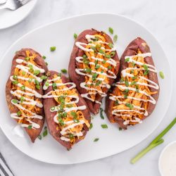 Buffalo chicken stuffed sweet potatoes on a plate with ranch dressing and green onions.