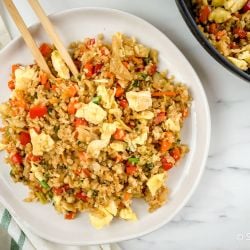 Cauliflower fried rice with cabbage, carrots, eggs, and green onions on a plate with chopsticks.