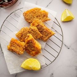Crispy baked fish with breading on a wire rack with lemons and salad.