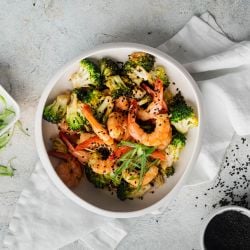 Firecracker shrimp and broccoli in a bowl with green onions and sesame seeds.