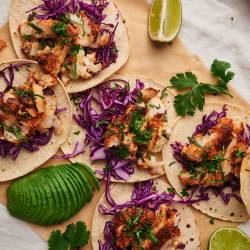 Fish tacos with flaky seasoned fish served in a corn tortilla with cilantro, shredded red cabbage, and limes. 