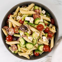 Greek pasta salad with tomatoes, cucumbers, black olives, feta cheese, and Greek dressing in a bowl. 