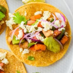 Vegetable tostadas on a plate with zucchini, eggplant, peppers, cheese, and avocado.