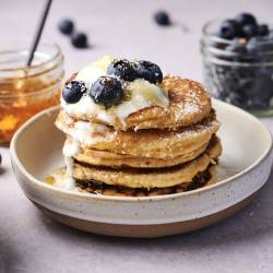 Low carb almond flour pancakes on a plate with blueberries, yogurt, and maple syrup.