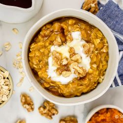 Pumpkin oatmeal with walnuts, maple syrup, and yogurt in a bowl with oats on the side.