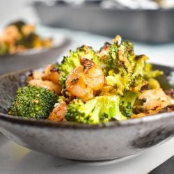 Garlic Roasted shrimp and broccoli in a bowl with shredded cheese, lemon, and red pepper flakes.