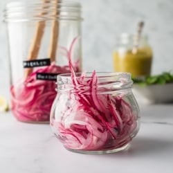 Pickled red onions in a glass jar with lime juice, vinegar, and peppercorns. 