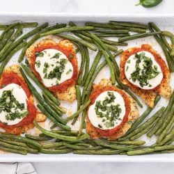 Healthy Chicken Parmesan with breaded chicken covered in sauce and cheese on a sheet pan with roasted green beans.