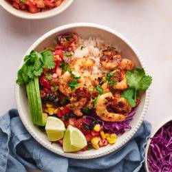 Shrimp taco bowls with cooked shrimp, avocado, rice, lime, cilantro, cabbage, corn, and pico de gallo in a white bowl.