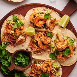 Shrimp tacos with slaw served on corn tortillas with avocado, lime, and fresh cilantro.