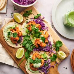 Shrimp tacos served on corn tortillas with avocado, cabbage, cilantro, lime wedges, and a creamy sauce. 