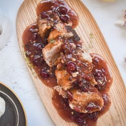 Slow cooker cranberry pork roast with sliced pork and a cranberry honey sauce on a wooden plate.