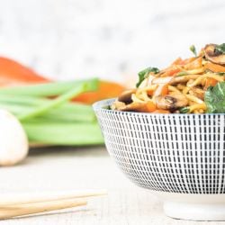 Spinach and Mushroom lo mein in a bowl with chopsticks picking up noodles.
