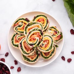 Turkey pinwheels with cream cheese, dried cranberries, cheddar cheese, lettuce, and tomatoes wrapped in a tortilla and sliced into pinwheels.