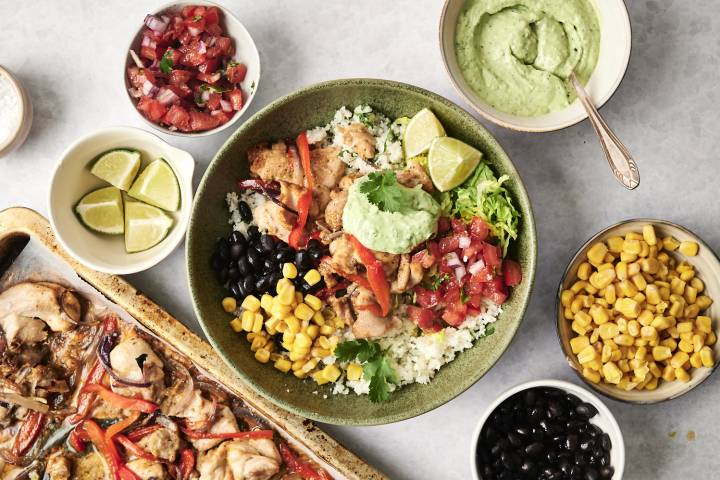 Chicken and cauliflower rice bowl with black beans, corn, salsa, avocado crema, and lime wedges.