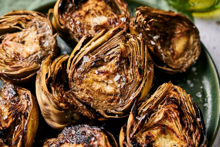 Grilled artichokes with flaky sea salt served on a plate with garlic butter.