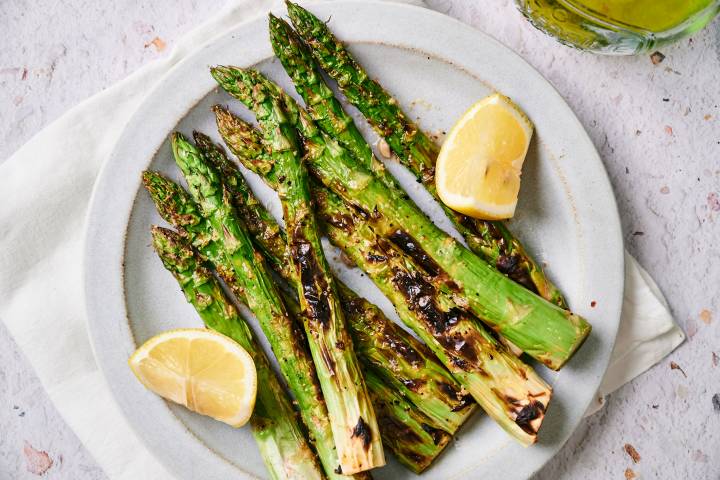 Grilled asparagus with charred edges on a plate with lemon, salt, and pepper.