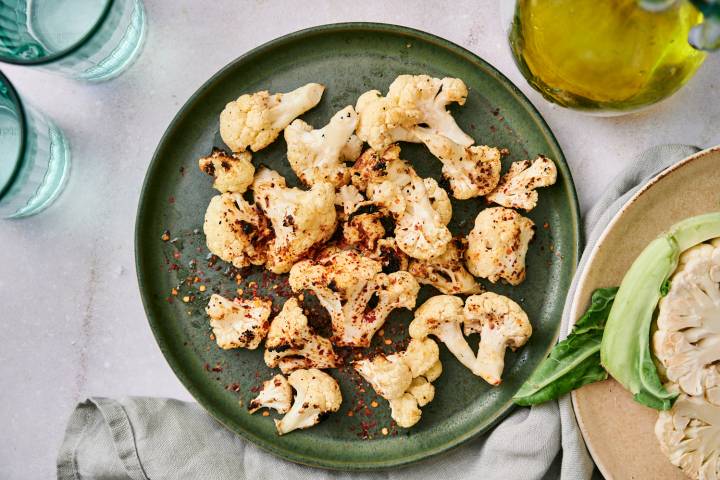 Grilled cauliflower with browned edges on a plate with red pepper flakes, salt, pepper, and olive oil.