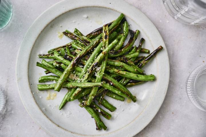 Grilled green beans served on a plate with fresh lemon, salt, and pepper.