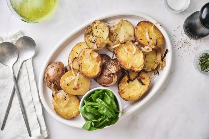 Grilled red potatoes with olive oil, salt, pepper, and onions served on a white plate.