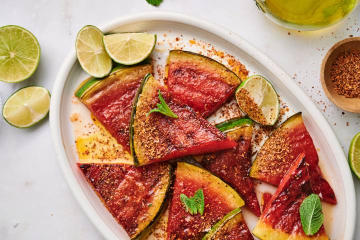 Grilled watermelon on a platter served with chili powder, lime wedges, and fresh mint.