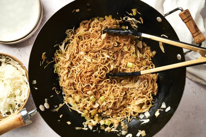 Healthy chow mein with cabbage, noodles, and celery in soy sauce in a wok.