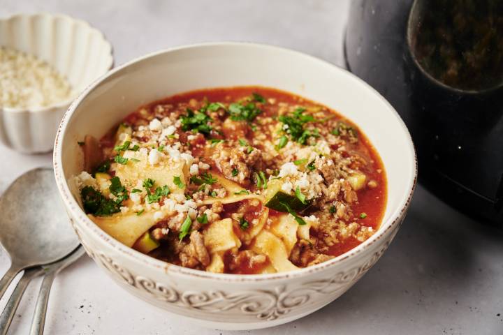 A bowl of lasagna soup with a rich tomato broth, ground meat, zucchini, and lasagna noodles, topped with parmesan cheese and fresh parsley.