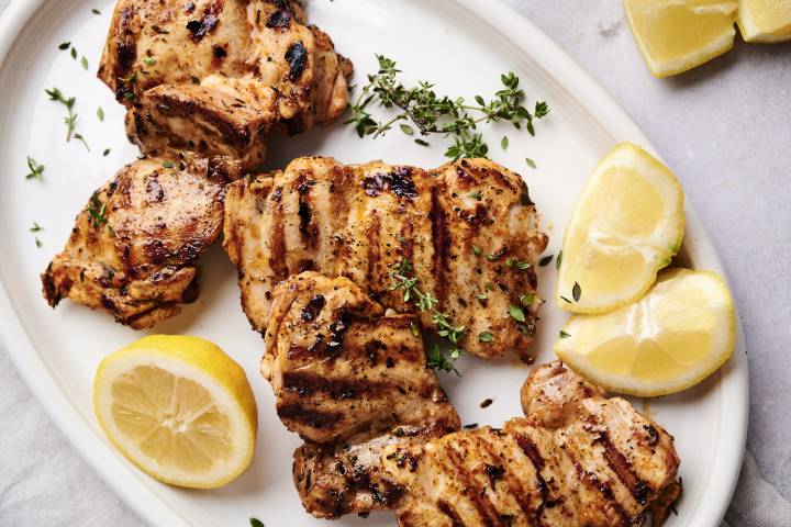 Lemon paprika chicken thighs served on a plate with lemon wedges and thyme.