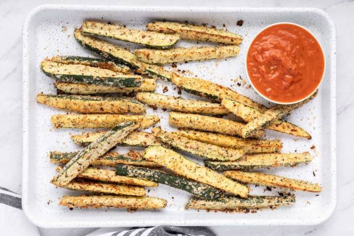 Low carb Parmesan zucchini fries with crispy edges served on a baking sheet with marinara sauce.