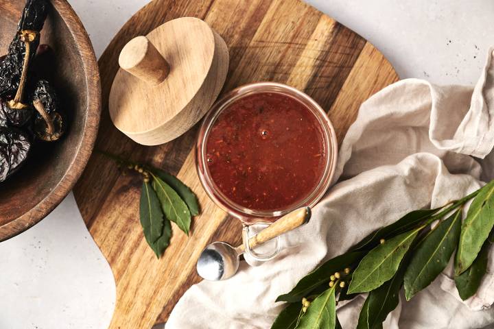 Mexican adobo sauce made with dried chilies and vinegar in a glass jar with a spoon.