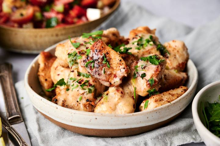 Sauteed lemon pepper chicken with creamy lemon sauce in a bowl with parsley and tomato salad on the side.