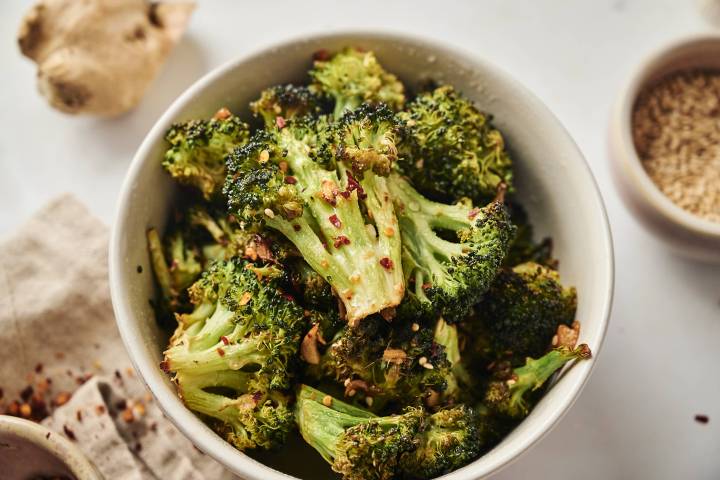 Sesame broccoli with sesame oil, sesame seeds, and soys sauce in a bowl with red pepper flakes and garlic.