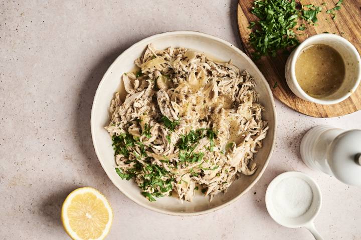 A plate of slow-cooked lemon garlic chicken, shredded and garnished with fresh parsley. 