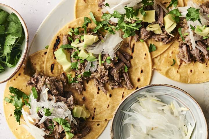 Shredded salsa verde beef served in corn tortillas, garnished with chopped onions, sauce, and fresh cilantro.