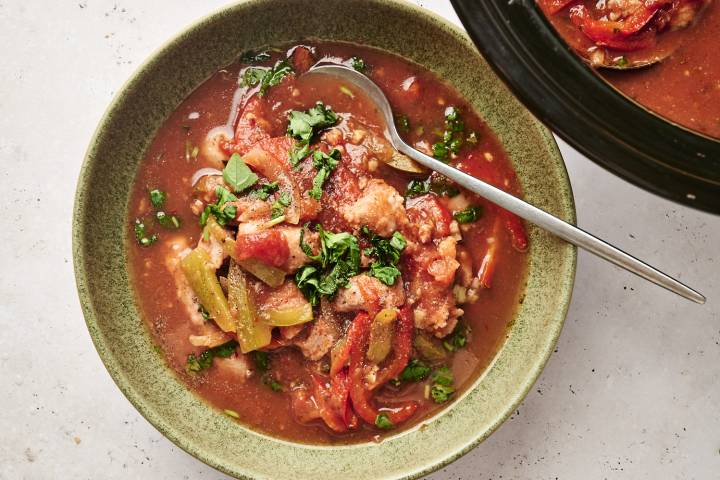 Bowl of slow-cooked sausage and peppers in tomato sauce, garnished with fresh herbs.