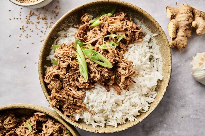 Shredded sesame beef over rice with green onion garnish.