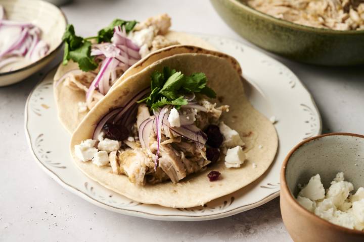 Shredded turkey tacos with red onion, cilantro, dried cranberries, and crumbled cheese on soft flour tortillas.