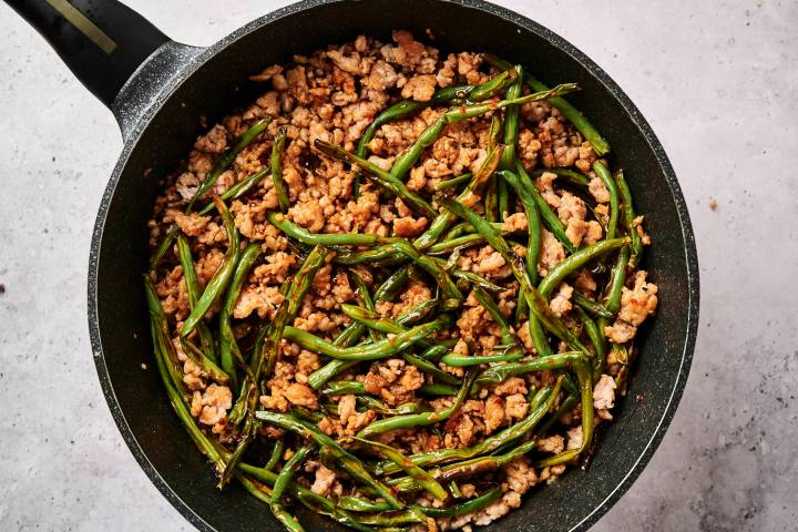 Ground turkey and green bean stir fry in a skillet with spicy sauce and chopsticks.