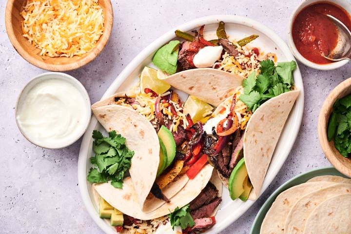 Steak fajitas with bell peppers, red onion, tender steak, sour cream, cheese, avocado, and cilantro in flour tortillas.