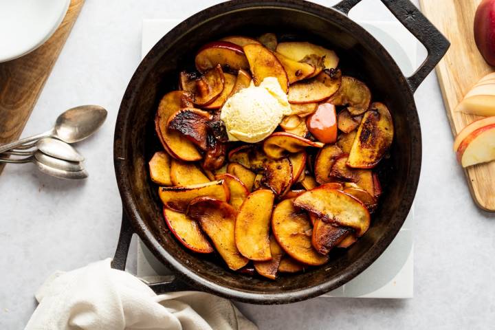 Stovetop cinnamon apples being served up in a cast iron skillet with spoons.