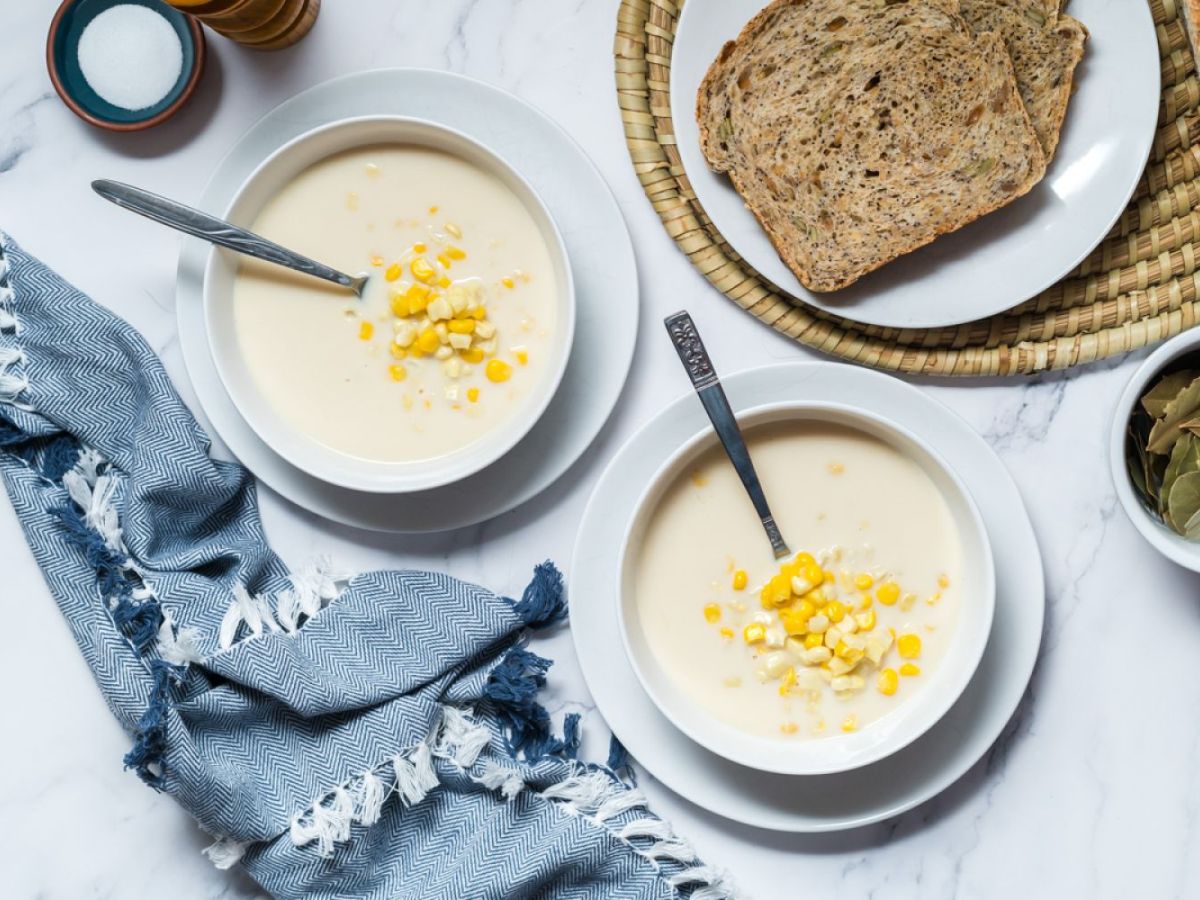 Corn chowder made with fresh corn, cauliflower, onions, milk, and spices in two bowls with bread on the side.