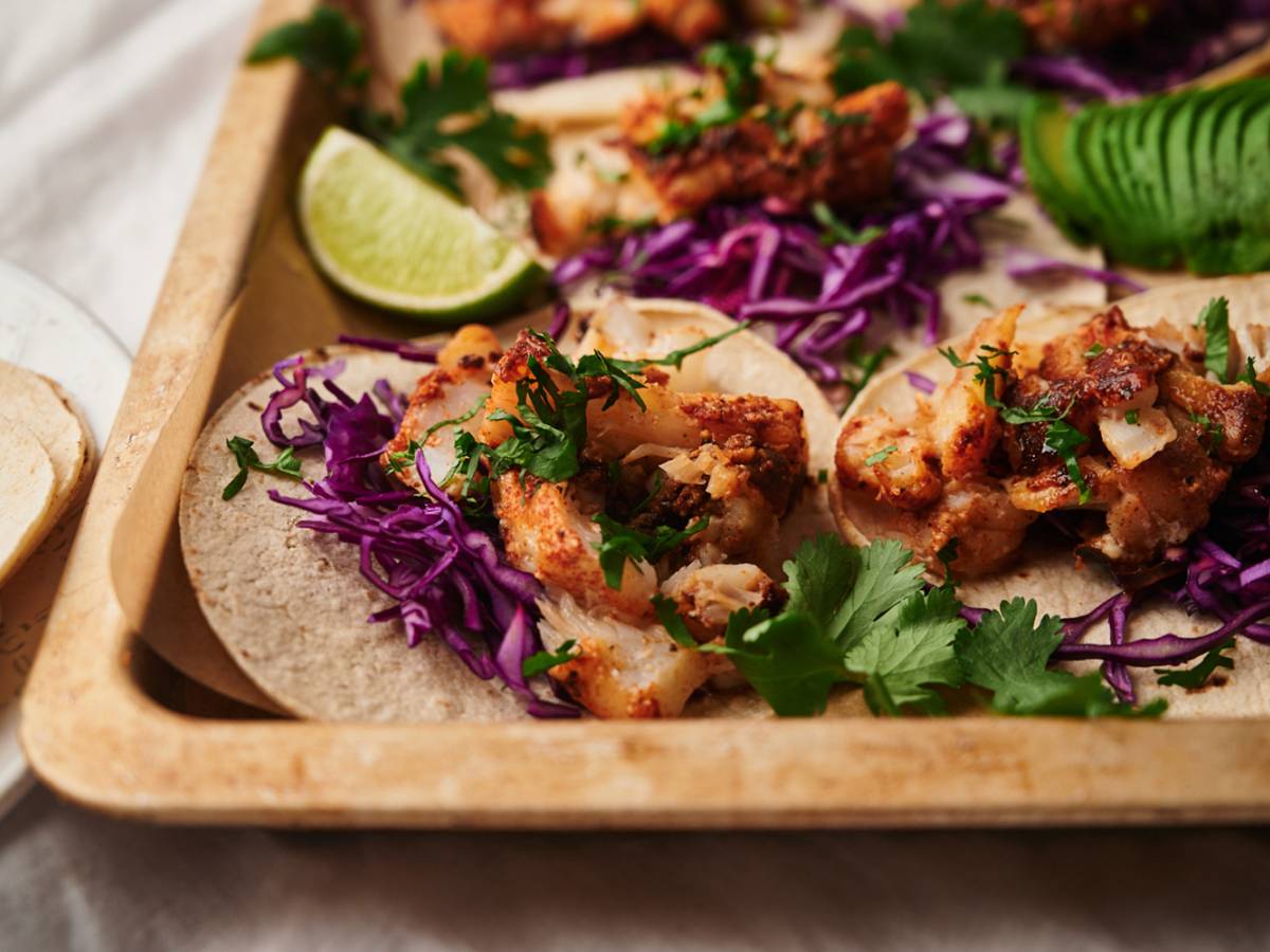 Fish tacos with flaky seasoned fish served in a corn tortilla with cilantro, shredded red cabbage, and limes.