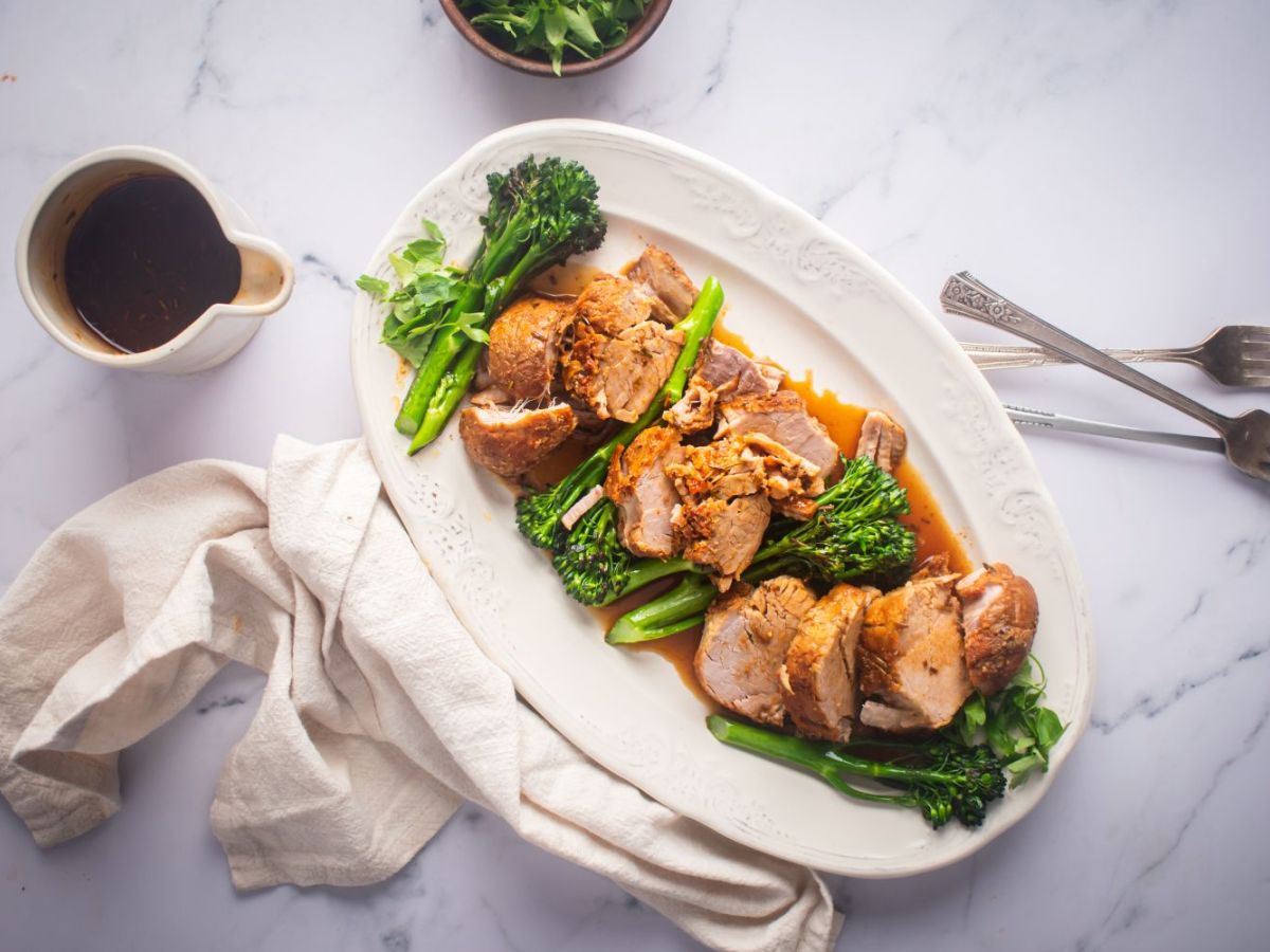 Slow cooker pork tenderloin with mustard sauce and broccolini on a white platter.