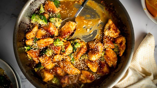 Stir fried orange chicken with broccoli in a heavy skillet with sesame seeds on top.