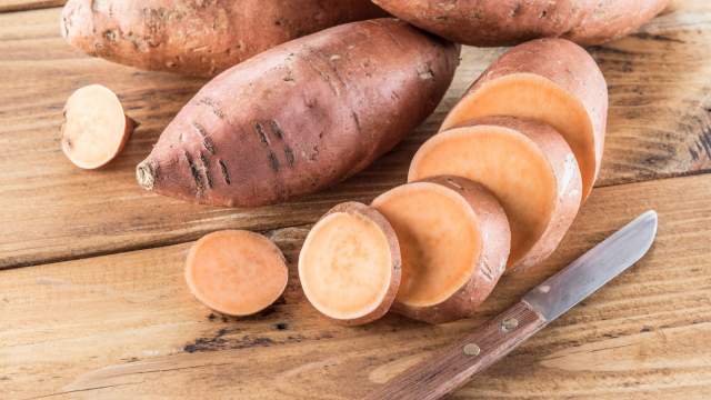 Sweet potato on a wooden cutting board with a knife.