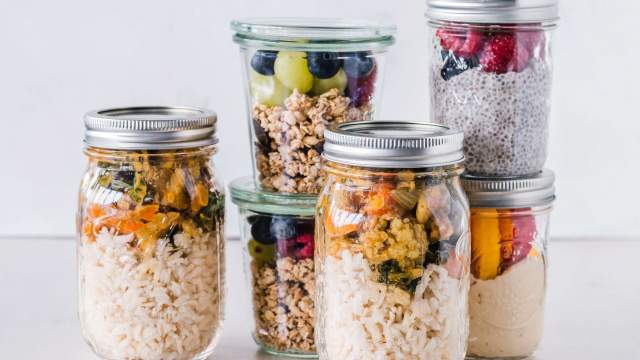 Healthy meal planning jars with salad, granola, hummus, brown rice, and ground chicken.