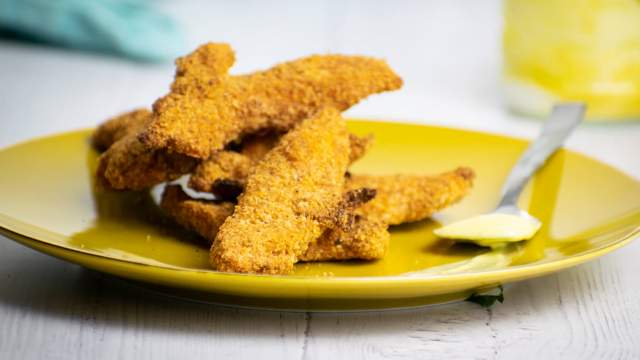 Almond chicken tenders piled on a plate with honey mustard.