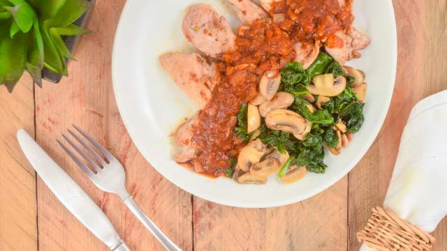 Balsamic chicken thighs with spinach and mushrooms on a plate with a napkin, fork, and knife.