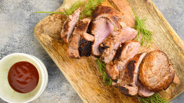 Barbecue rubbed pork tenderloin sliced on a wooden board with rosemary.
